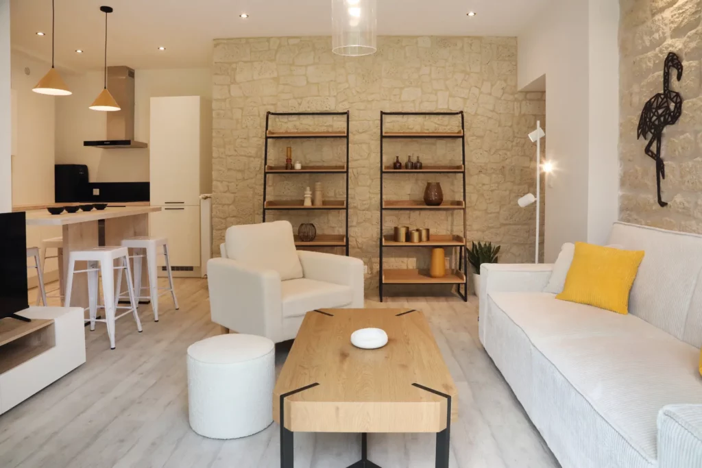 Rénovation d'un T2 à Chantilly par Ilot Archi : pièce de vie ouverte avec mur en pierres apparentes et cuisine américaine.