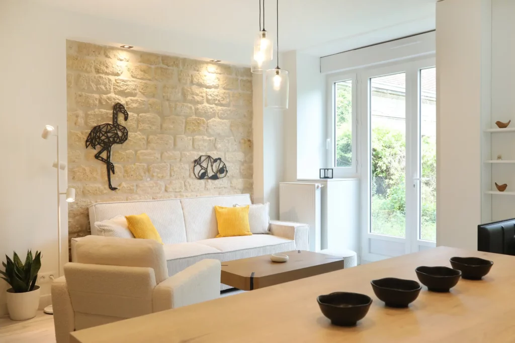 Vue depuis l'îlot de cuisine sur le salon cosy et lumineux d'un appartement T2 décoré par Ilot Archi à Chantilly.