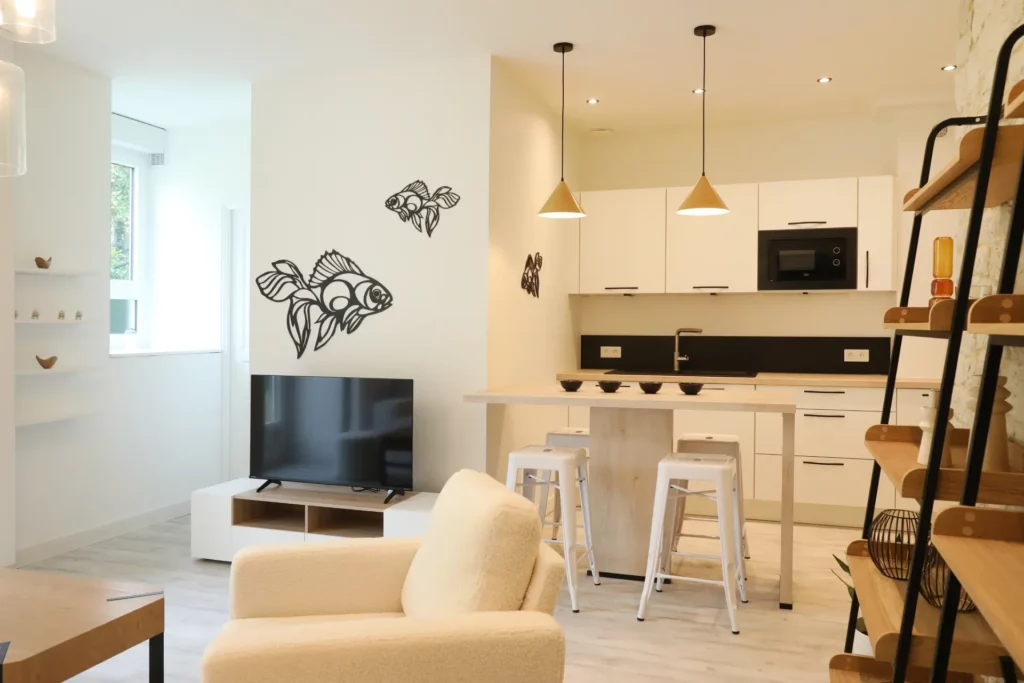 Aménagement intérieur d'un T2 à Chantilly par Ilot Archi avec coin TV, étagères industrielles et cuisine en arrière-plan.