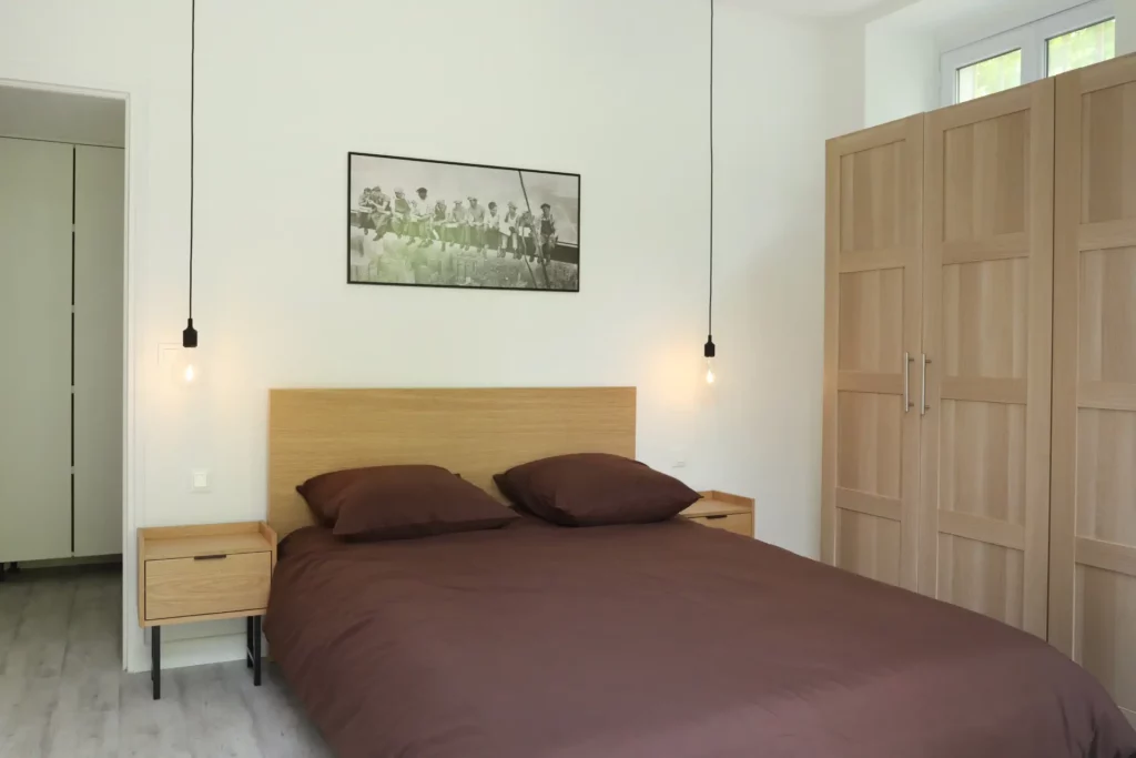 Suite parentale optimisée dans un appartement à Chantilly par Ilot Archi, associant rangement en bois et éclairage suspendu.