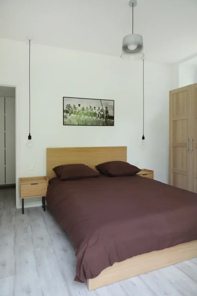 Espace nuit sobre et design aménagé par Ilot Archi avec linge de lit marron et tables de chevet coordonnées.