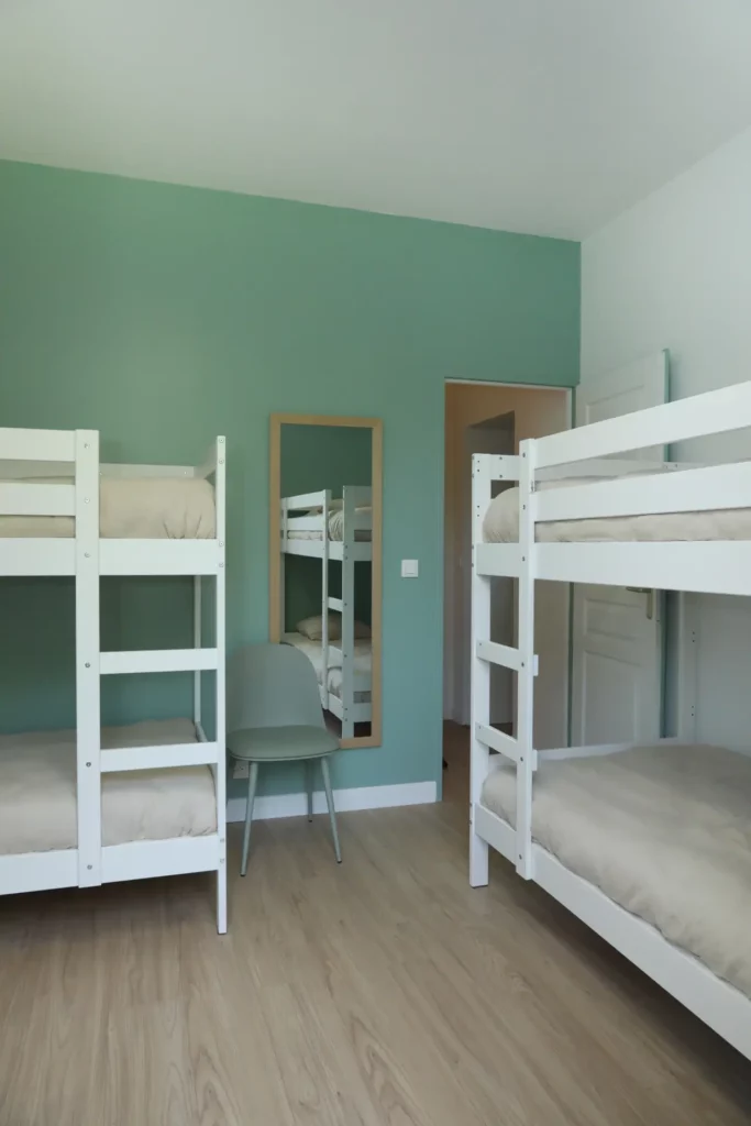 Rénovation d'une chambre d'enfants pour 4 personnes par Ilot Archi à Chantilly avec mur vert sauge et lits superposés blancs.