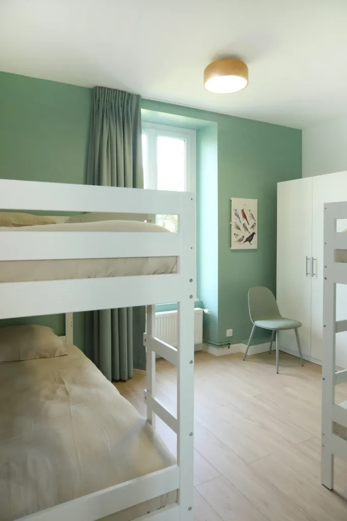 Décoration d'une chambre d'enfants verte et bois par Ilot Archi avec dressing blanc, lits superposés et lumière naturelle.