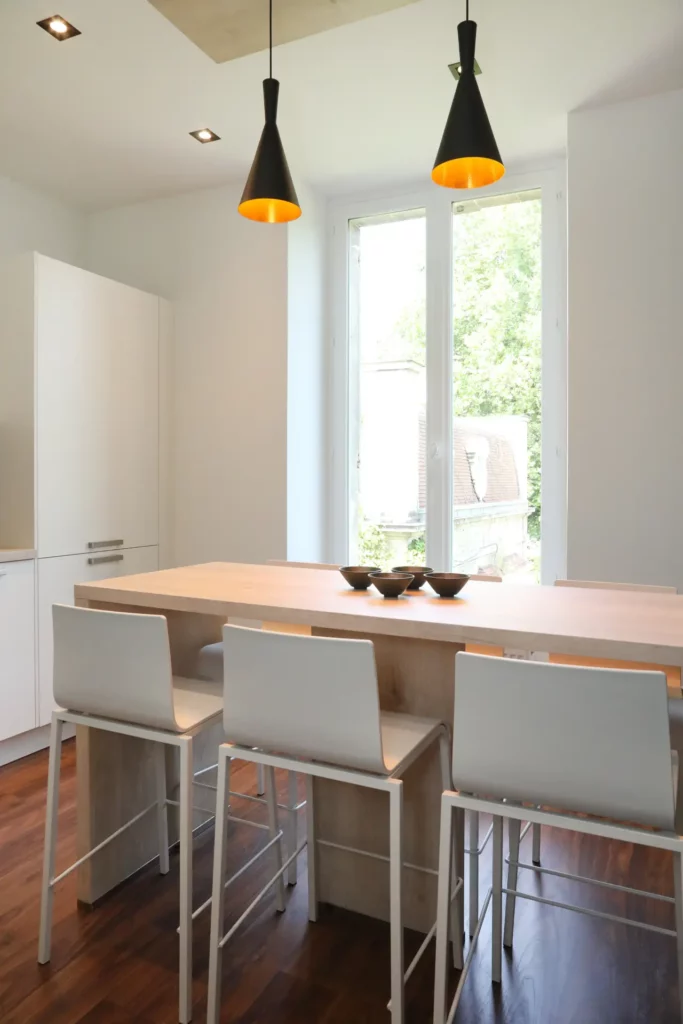 Table haute sur mesure en bois clair et tabourets blancs conçus par Ilot Archi pour la cuisine d'un grand appartement à Chantilly.