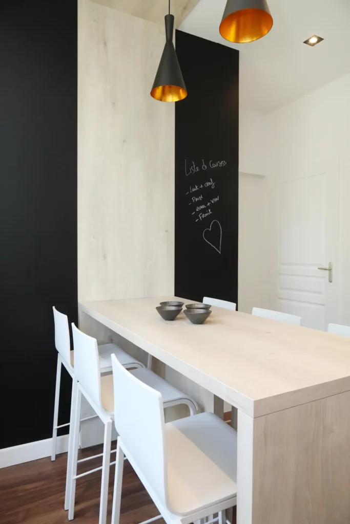 Coin repas d'une cuisine rénovée par Ilot Archi à Chantilly avec mur peint en peinture tableau noir ardoise et suspensions noires.