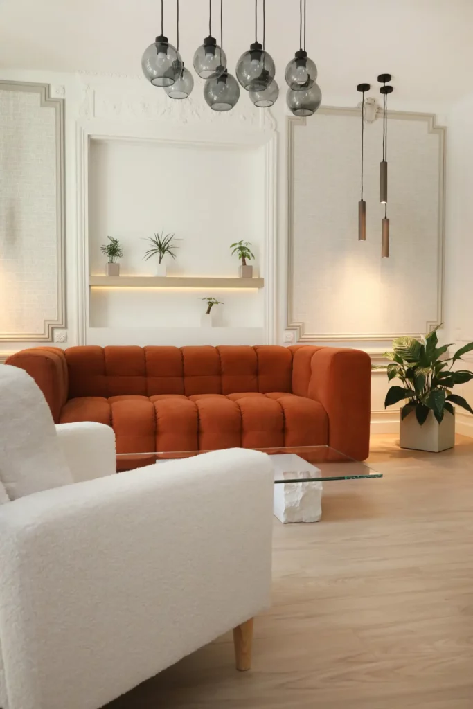 Salon d'un grand appartement T5 à Chantilly rénové par Ilot Archi avec canapé terracotta, suspensions en verre et éléments d'époque.