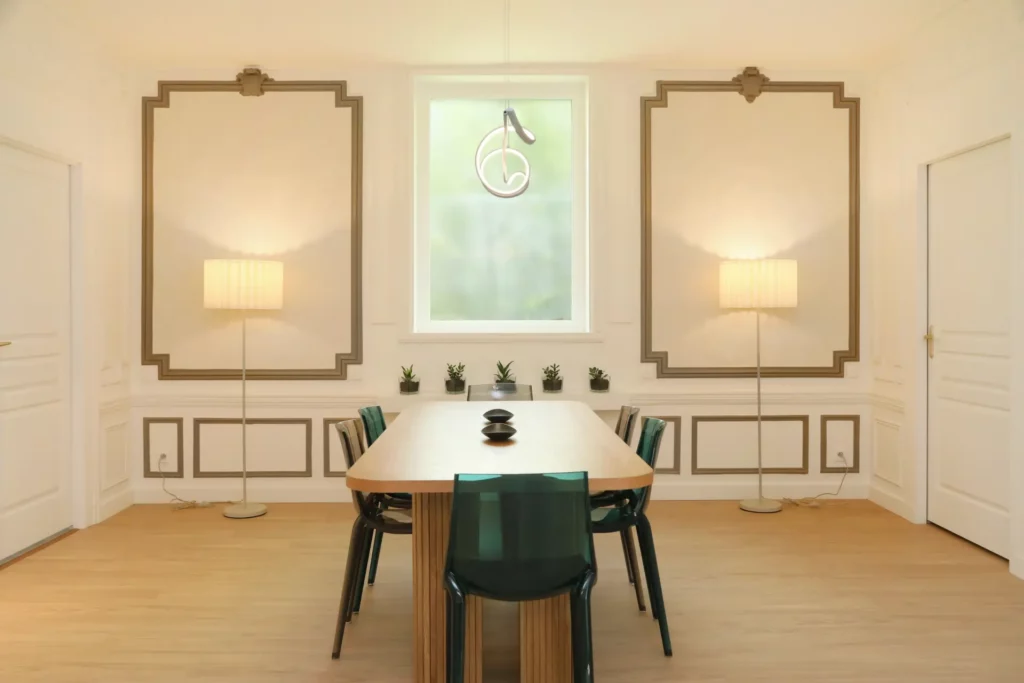 Grande salle à manger bourgeoise rénovée par Ilot Archi à Chantilly avec moulures murales, lampadaires design et grande table en bois.