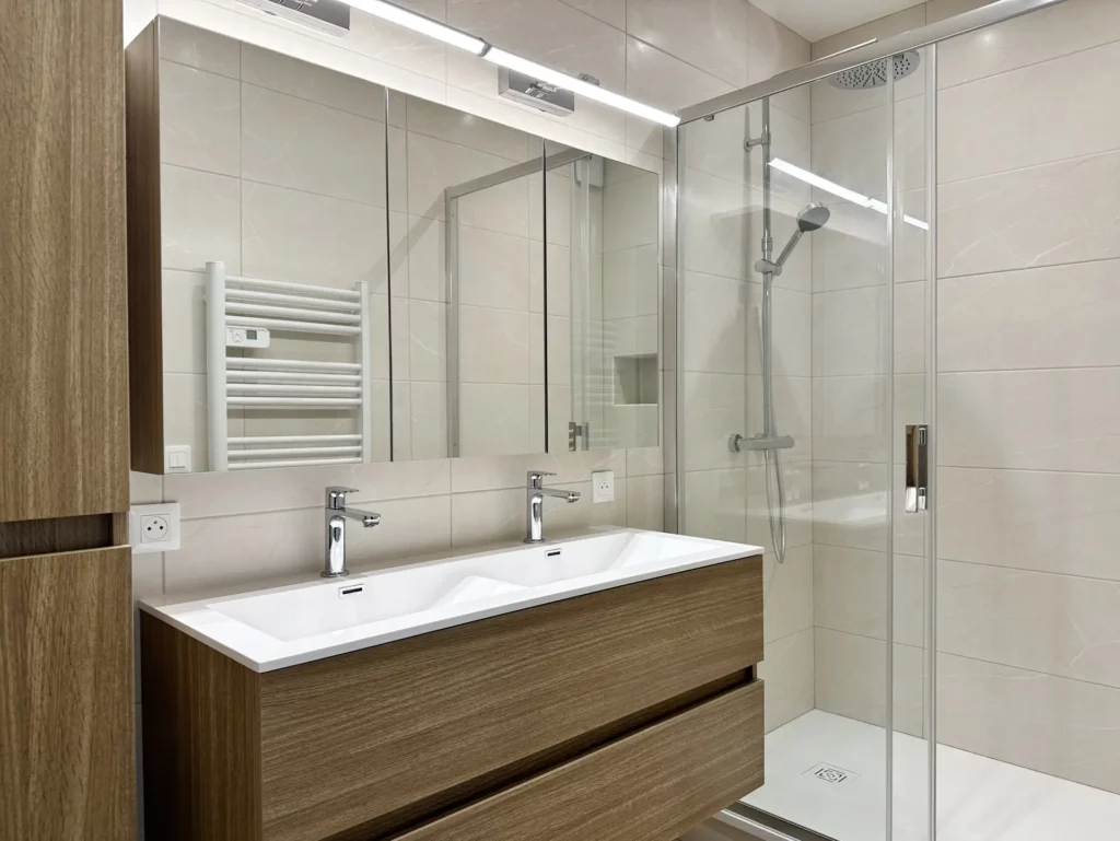 Rénovation d'une salle d'eau moderne en bois et beige par Ilot Archi avec grande douche à l'italienne et meuble double vasque suspendu.